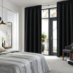 Rideaux noirs occultants posés dans une chambre moderne avec lit gris, baie vitrée et accès à un balcon verdoyant.
