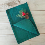 Un journal relié en vert orné de pommes de pin et de baies rouges, décoré sur une surface en bois.