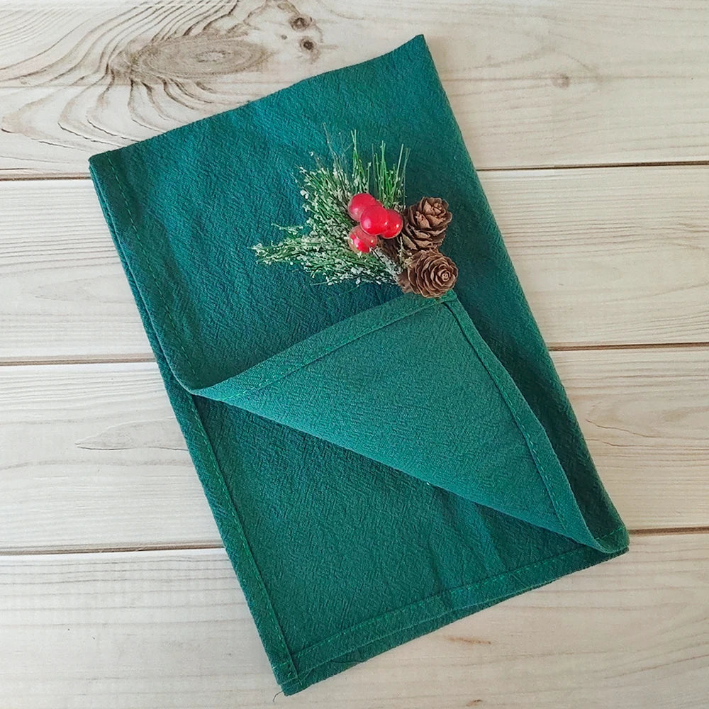 Un journal relié en vert orné de pommes de pin et de baies rouges, décoré sur une surface en bois.