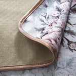 Cette image montre un coussin de style floral avec des motifs gris foncés et roses, entouré d'une bordure marron.