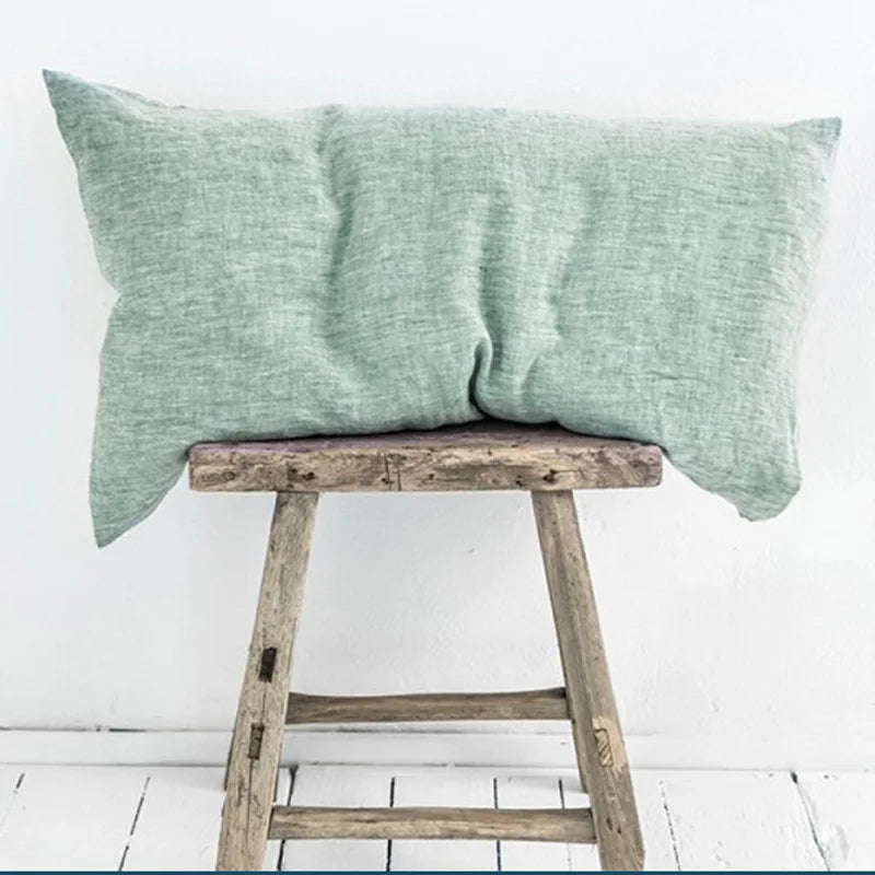 Coussin en lin vert posé sur un tabouret rustique en bois, créant une ambiance sereine et naturelle.