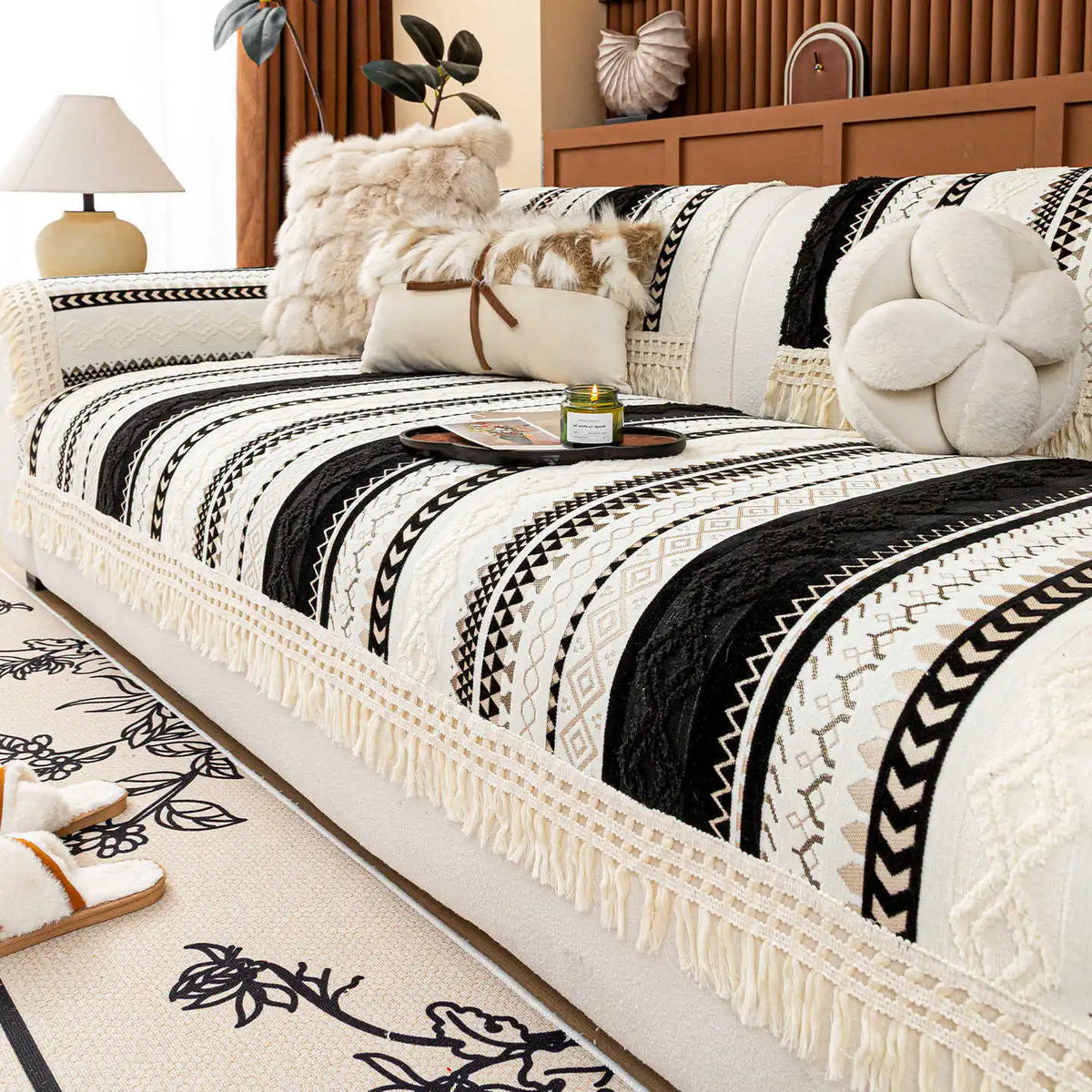 Lit couvre-lit décoré de motifs géométriques noirs et blancs avec des franges, entouré d'accessoires d'intérieur dans un style cosy et confortable.