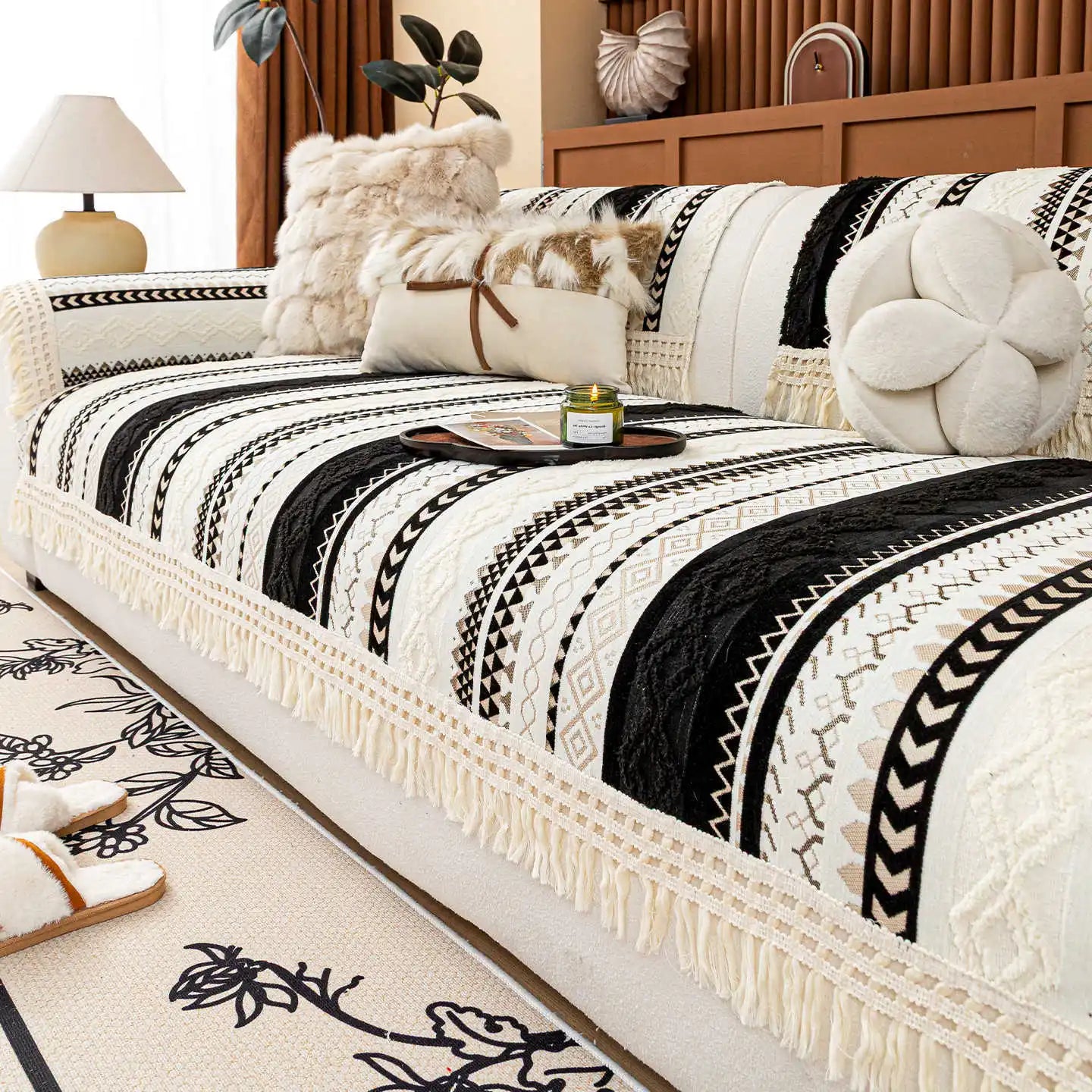 Lit couvre-lit décoré de motifs géométriques noirs et blancs avec des franges, entouré d'accessoires d'intérieur dans un style cosy et confortable.