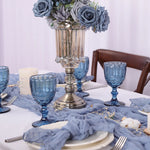 Table de salle à manger élégante décorée de fleurs grises, de bougeoirs et de verres bleus, créant une ambiance chaleureuse et raffinée.