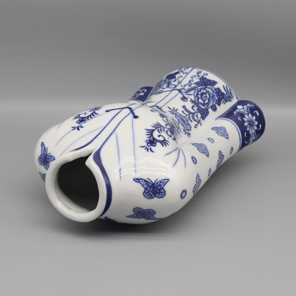 Vase décoratif blanc et bleu avec des motifs floraux et des papillons.