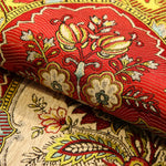 L'image montre un motif floral coloré et détaillé sur un tissu, mettant en valeur des tons rouge vif, jaune et beige dans un style traditionnel.