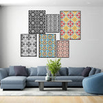 Ensemble de cadres décoratifs muraux avec des motifs géométriques variés dans les tons de noir, blanc, rouge et bleu, disposés sur un mur blanc au-dessus d'un canapé gris foncé dans un salon lumineux.