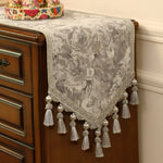Ce meuble antique est recouvert d'un chemin de table décoré de motifs floraux et de pompons blancs, créant une ambiance vintage et élégante dans la pièce.