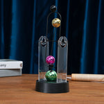 pendule newton sphères colorées structure métallique support transparent base circulaire décoration cinétique moderne