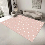 Un tapis rose clair avec des étoiles blanches dans un salon moderne et épuré, avec un canapé et des coussins gris, créant une ambiance apaisante et contemporaine.