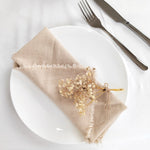 Une nappe beige en lin avec un bouquet de fleurs séchées est posée sur une assiette blanche avec une fourchette et un couteau en métal.