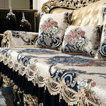 Cette image montre une décoration de chambre de luxe, avec un design vintage et ornementé. Elle met en valeur des coussins et une couverture brodée de motifs floraux classiques sur un canapé doré.