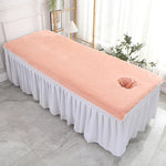 Un lit de massage rose pâle avec une couverture élégante, dans un cadre spacieux et lumineux.