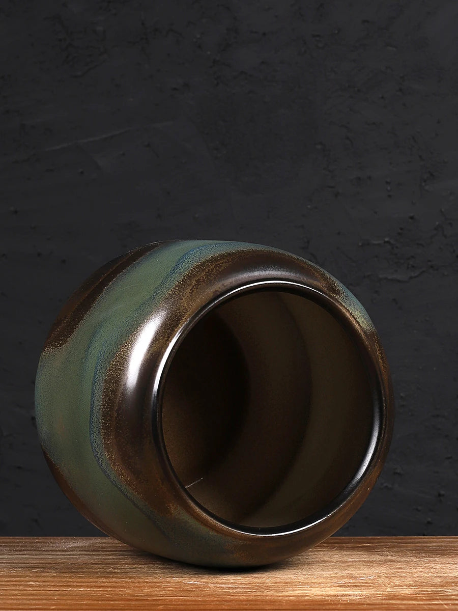 Un vase vintage en céramique, aux teintes de vert, de brun et de dorée, posé sur une surface en bois.