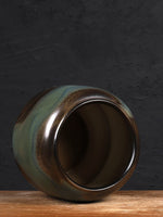 Un vase vintage en céramique, aux teintes de vert, de brun et de dorée, posé sur une surface en bois.