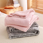 Pile de serviettes roses et grises en textile doux et texturé, disposées sur une surface blanche, créant une atmosphère confortable et accueillante.