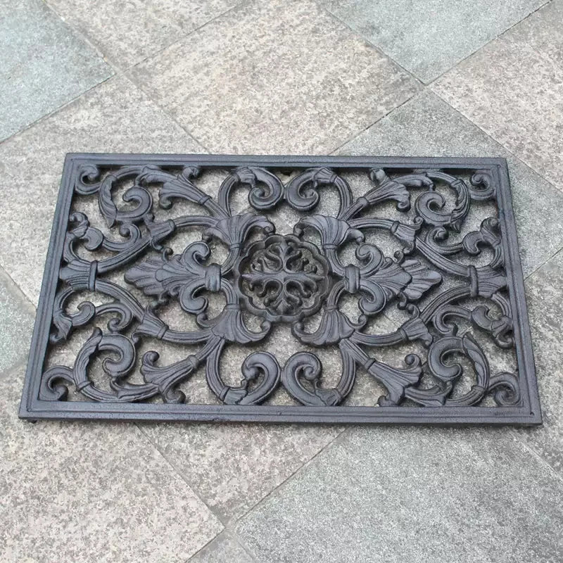 Paillasson rectangulaire en fonte noir posé devant une porte d'entrée