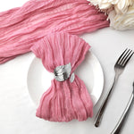 Une serviette de table rose aux plis doux et élégants, avec une décoration en métal en forme de plume, accompagnée d'une fourchette et d'un couteau sur une surface blanche.