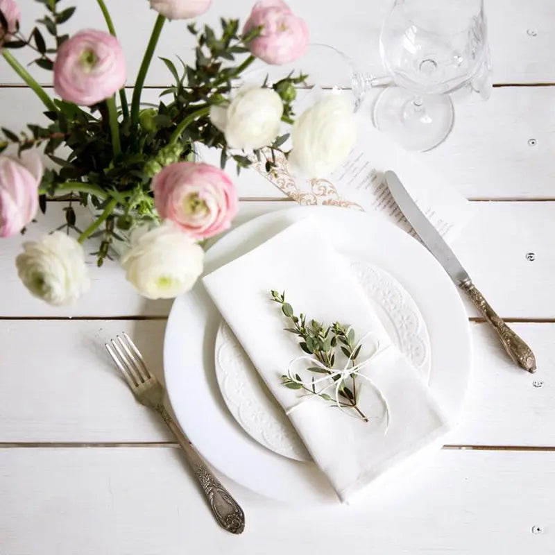 Élégante table blanche avec un bouquet de fleurs roses et blanches, assiettes et couverts sur un fond de bois blanc.