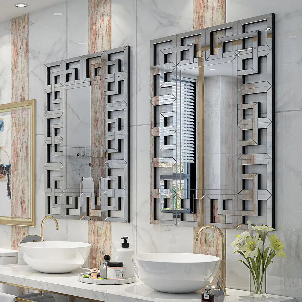 L'image montre une salle de bain élégante et moderne, avec des lavabos blancs sur un plan de travail et des miroirs décoratifs avec un motif géométrique en métal argenté qui rappelle l'architecture contemporaine.