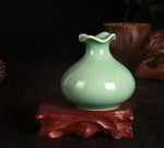 Vase en céramique vert pastel posé sur un support en bois rougeâtre.