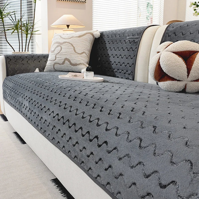 Un canapé gris confortable et douillet avec des motifs géométriques décoratifs, orné de coussins moelleux et d'un pouf en peluche, placé dans un bel intérieur lumineux.