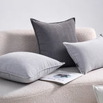 L'image montre des coussins décoratifs gris et blancs disposés sur un canapé moelleux, avec un livre placé à côté.