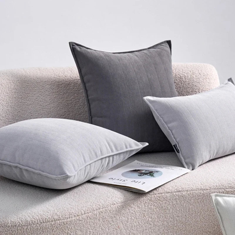 L'image montre des coussins décoratifs gris et blancs disposés sur un canapé moelleux, avec un livre placé à côté.