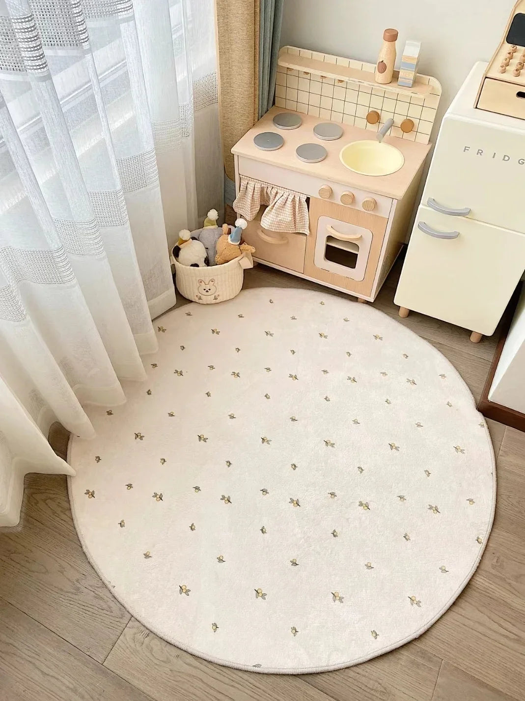 Une pièce confortable et accueillante, avec un sol en bois, des rideaux et un tapis rond à motifs délicats, complétée par du mobilier enfantin, comme une cuisinière jouet et un panier de peluches.
