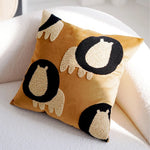 Coussin décoratif carré avec motif de yeux ou de monstres sur fond jaune, un élément de design amusant et ludique pour agrémenter un canapé ou un lit.