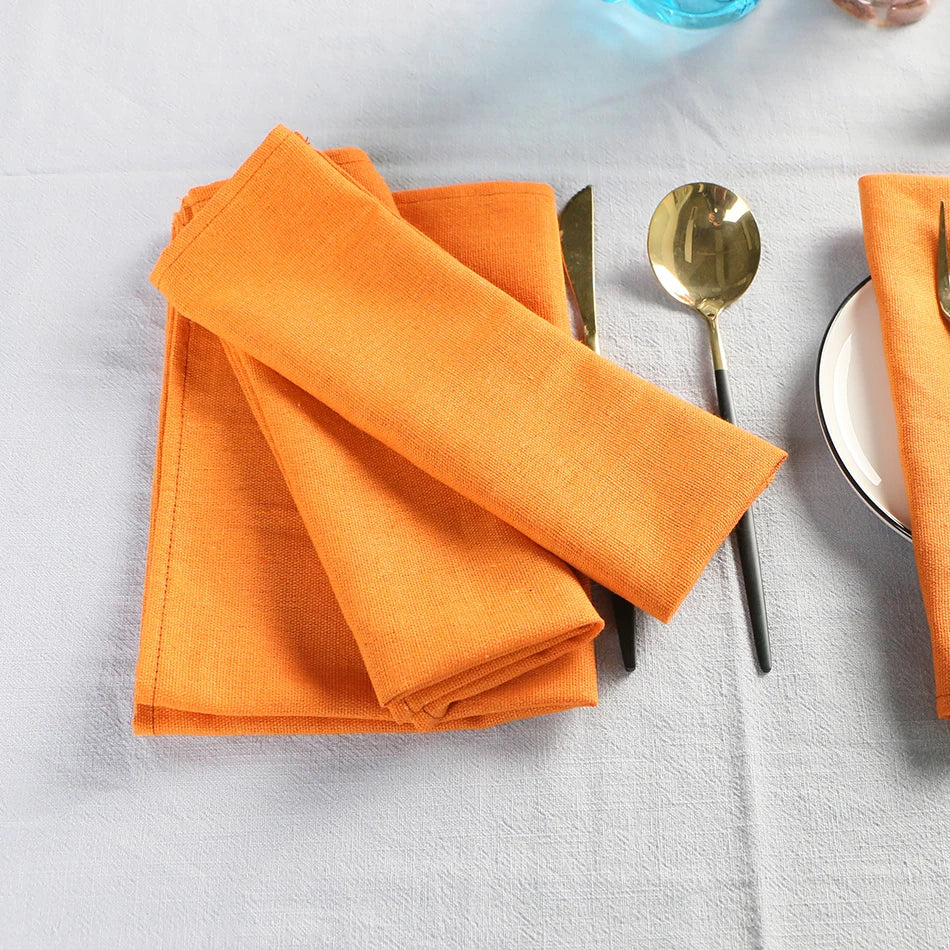 Des serviettes de table de couleur orange vif sont disposées sur une surface blanche, accompagnées de couverts dorés.