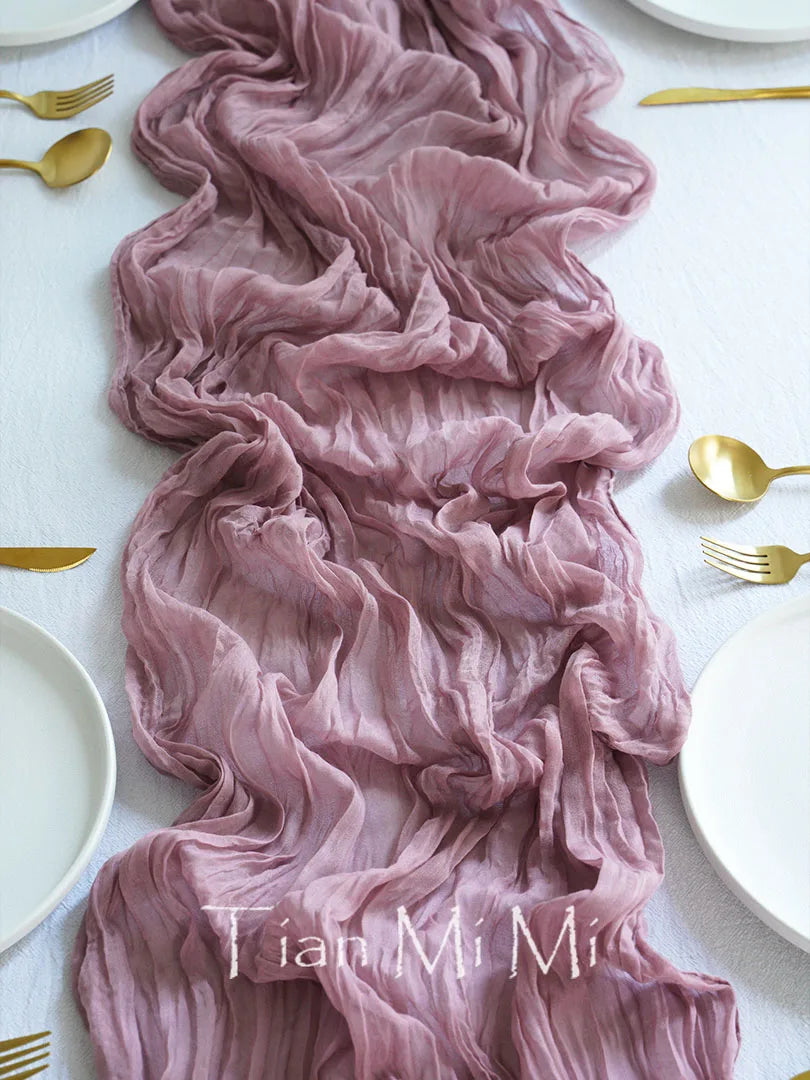 Un somptueux chemin de table rose pâle à froissures élégantes, accompagné d'accessoires dorés, créant une atmosphère sophistiquée et raffinée.