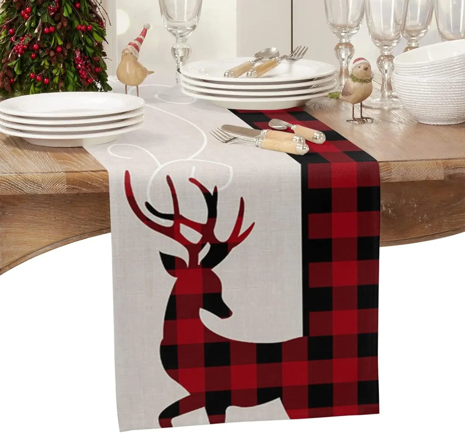 Table avec des assiettes blanches, une décoration de Noël avec des cerfs rouges et noirs sur un chemin de table à carreaux rouges et noirs, des verres et des couverts.