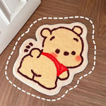 Tapis en forme d'ours mignon avec un foulard rouge, posé sur un sol en bois.