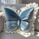 Coussin bleu en forme de papillon posé sur un fond blanc texturé.