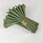Serviettes de table vert olive pliées avec un élégant anneau décoratif doré.