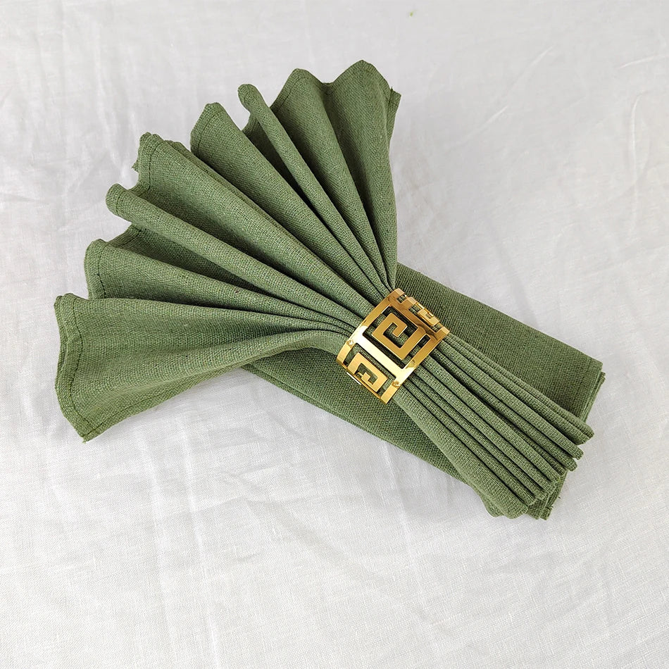 Serviettes de table vert olive pliées avec un élégant anneau décoratif doré.