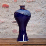 Un vase en céramique bleu foncé avec des motifs texturés, posé sur une table en bois dans un environnement intérieur.