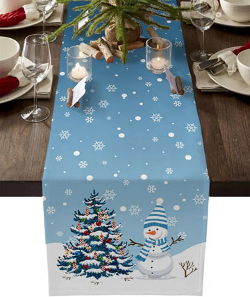 Une table de fête hivernale décorée avec un arbre de Noël illuminé, un bonhomme de neige et des flocons de neige sur fond bleu.