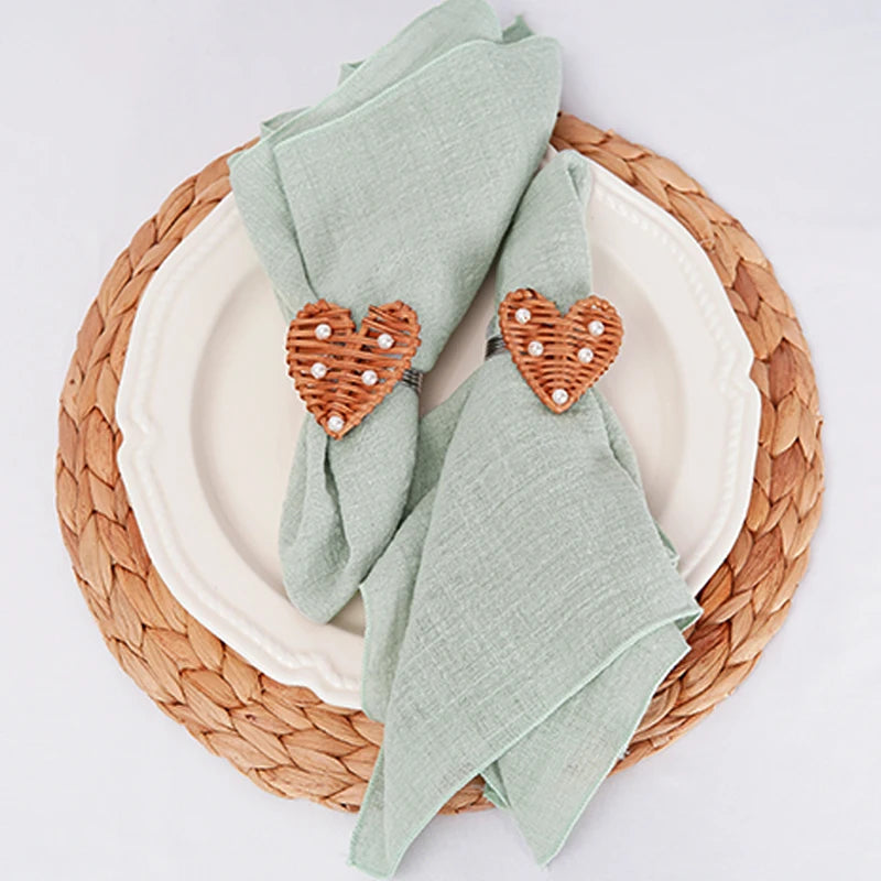 Assiette en céramique blanche avec serviettes de table vertes et accessoires décoratifs en forme de cœur orange sur un napperon tressé de couleur naturelle.