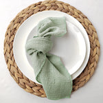 Une serviette de table en lin naturel, enroulée avec élégance sur une assiette posée sur un napperon en fibres tressées.