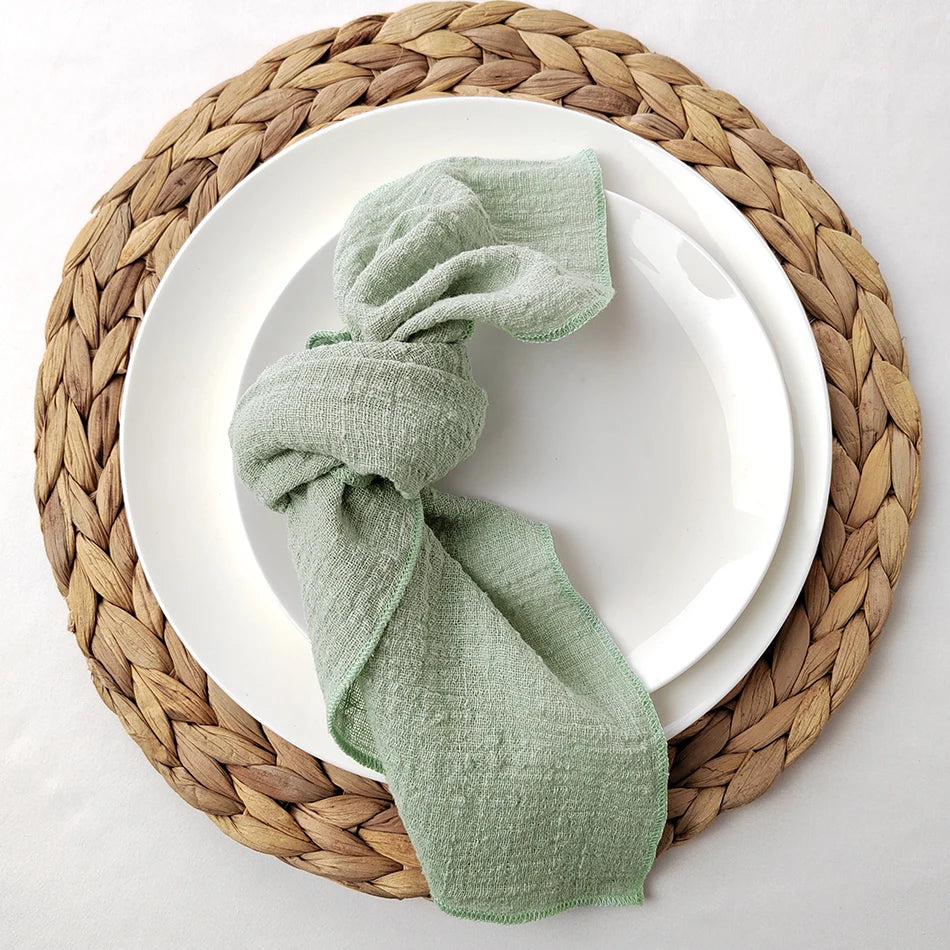 Une serviette de table en lin naturel, enroulée avec élégance sur une assiette posée sur un napperon en fibres tressées.