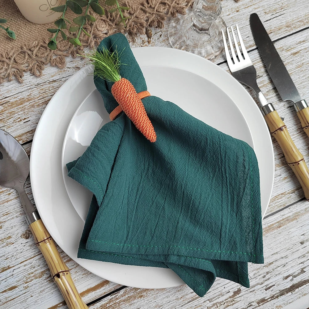Serviette pliée de couleur verte avec un motif de carotte, placée sur une assiette blanche avec des couverts en bois sur une table en bois.