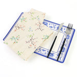 Assiette à motifs floraux bleus et blancs avec serviette assortie, entourée d'ustensiles de table.