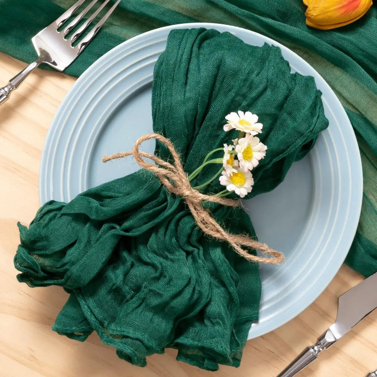 Une jolie serviette verte ornée de fleurs de marguerite, posée sur une assiette avec des couverts, créant une belle mise en scène pour une table de fête.