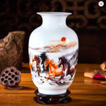 Cette image montre un vase en porcelaine blanche orné d'une scène peinte de chevaux sauvages galoppant sur un paysage montagneux avec un coucher de soleil en arrière-plan.