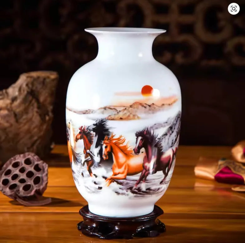 Cette image montre un vase en porcelaine blanche orné d'une scène peinte de chevaux sauvages galoppant sur un paysage montagneux avec un coucher de soleil en arrière-plan.