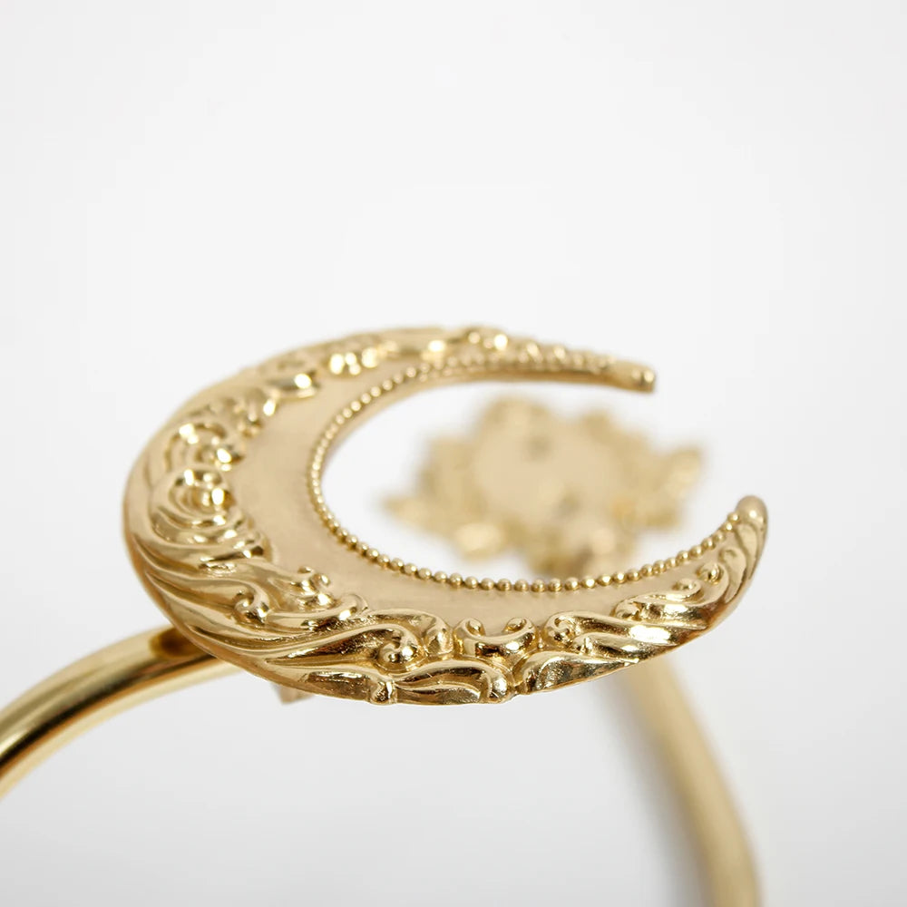 Bague dorée ornée de motifs décoratifs sculptés avec un élément central en forme de lune.