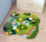 Un tapis décoratif en pompons de diverses teintes vertes, jaunes et roses, représentant un paysage naturel avec des arbres, des fleurs et des plans d'eau.