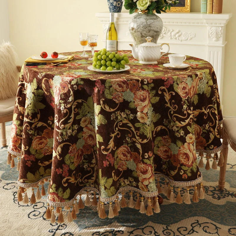 Cette image montre une table décorée avec un élégant napperon de style vintage orné de motifs floraux et de glands sur ses bordures. La table accueille divers éléments comme une théière, un vase de fleurs, une bouteille de vin et des raisins verts.